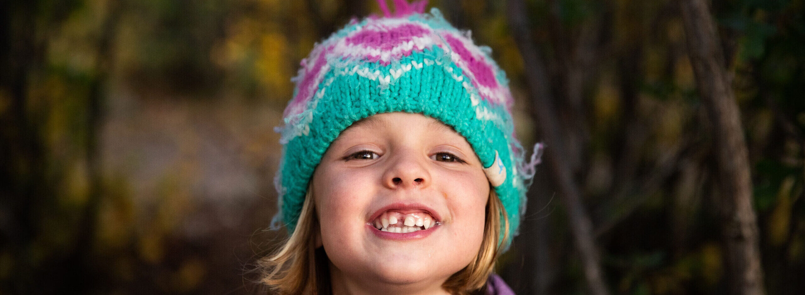 This up-close photo captures a girl wearing a vibrant purple and teal crocheted beanie, her big smile reflecting pure happiness.