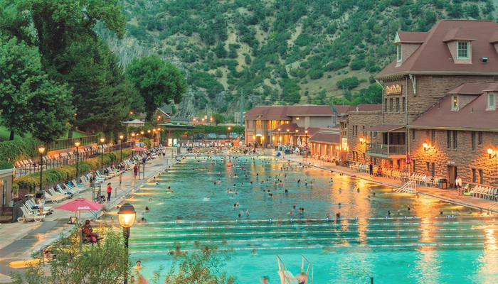 This photo captures the serene charm of Glenwood Hot Springs pool as seen from the pedestrian bridge in Glenwood Springs during the evening.