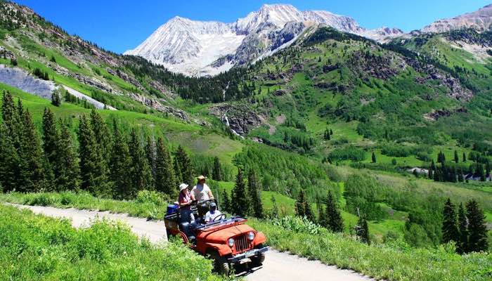 This is a photo of a jeep ascending a dirt road to Crystal Mill. The open-air design of the jeep provides panoramic views for both the guide and passengers. Against a backdrop of snow-covered mountains and lush forests, this scene encapsulates the timeless allure of Crystal Mill and the scenic journey to this historic site.