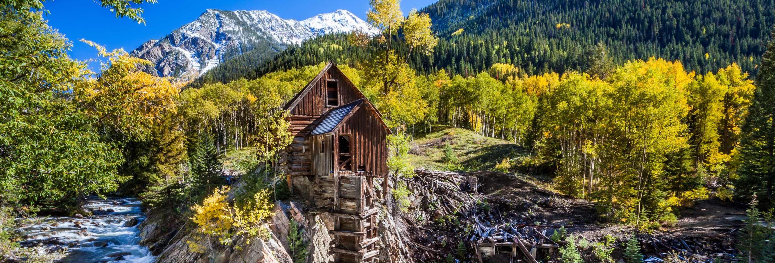 Capturing the timeless beauty of the old wooden Crystal Mill, this photo is framed by a lush forest with the tranquil Crystal River flowing beneath. Majestic mountains grace the distant horizon.
