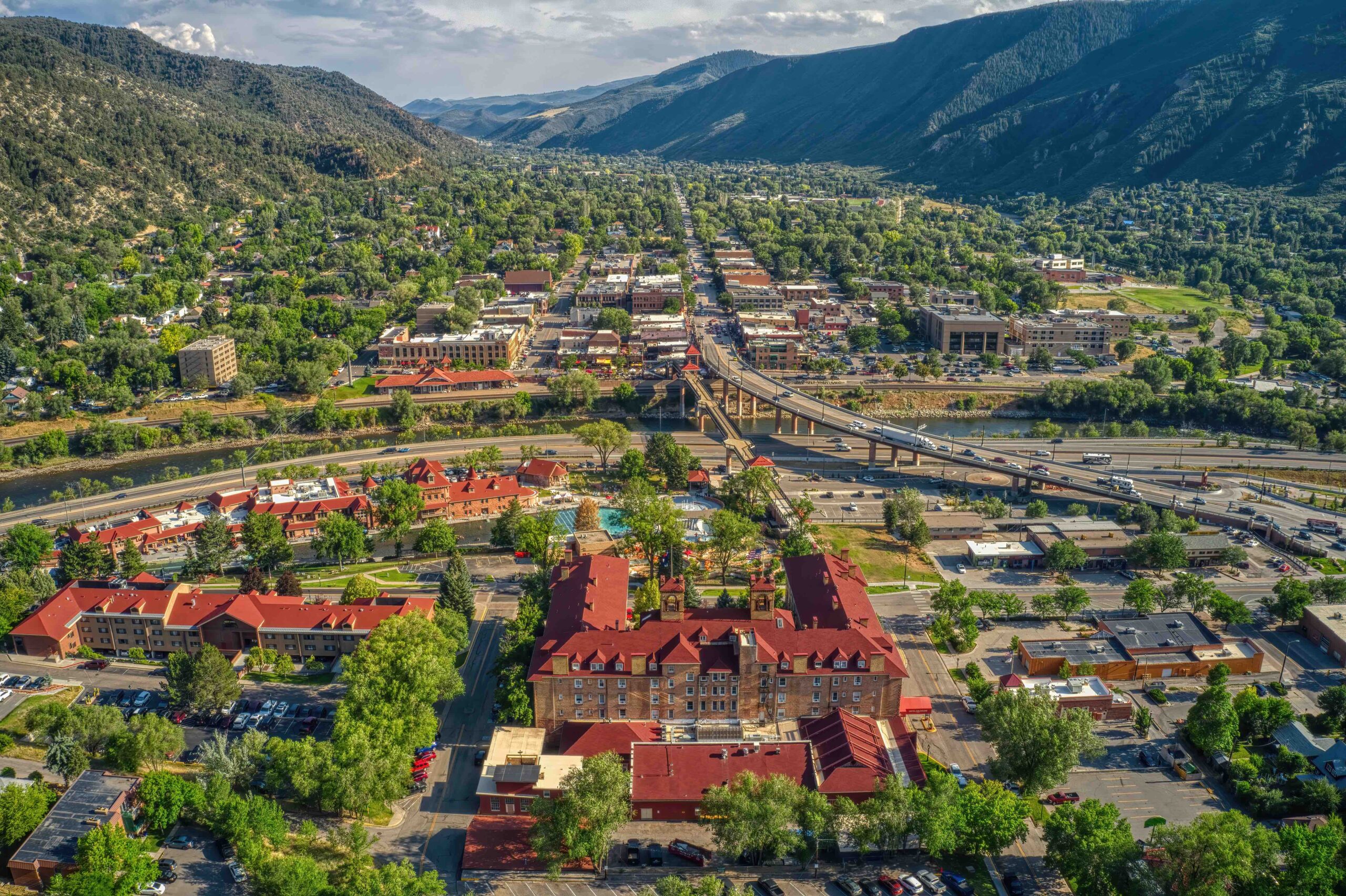 An elevated perspective of downtown Glenwood Springs. You can see many businesses, cars, and the large Glenwood Hot Springs Pool.
