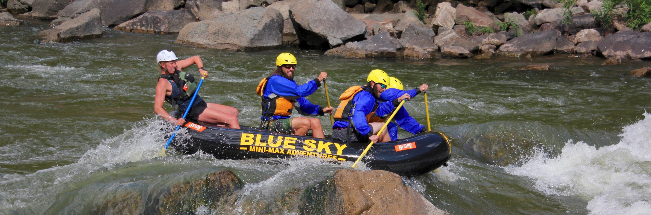 In this captivating image, three individuals, guided by their expert leader, skillfully navigate a Mini Max through the exhilarating Class III waters. As they paddle around a prominent rock situated in the midst of the scene, the photo encapsulates the thrill and teamwork involved in conquering challenging river rapids.