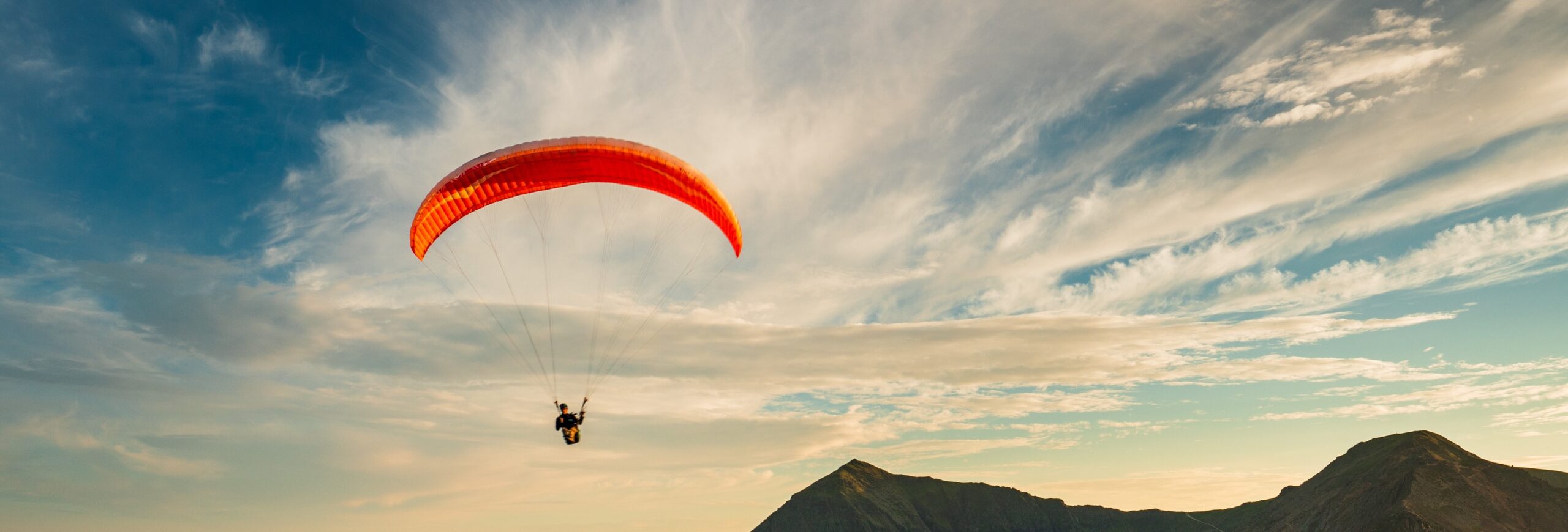 This captivating photo freezes a solitary paraglider in mid-soar against the expansive sky. The distinctive dark mountain peaks are visible, creating a scenic backdrop against the light, airy sky.
