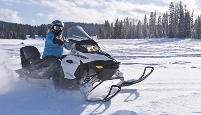 Experience the thrill of winter adventure with this captivating photo of a woman confidently riding a snowmobile. Dressed in winter gear, including gloves, helmet, and snow goggles, she skillfully navigates the snowy terrain. The forest forms a picturesque backdrop, and snow blows dynamically from the snowmobile as she speeds through the winter wonderland.