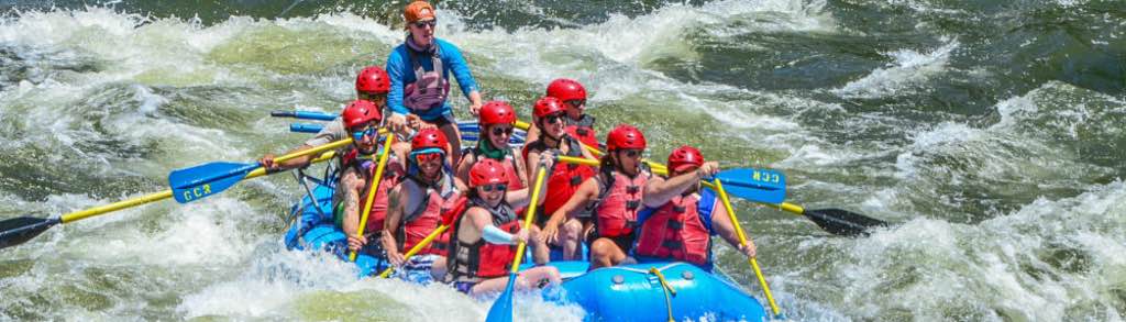 In this captivating image, a guide expertly navigates a full boat of guests through the exhilarating Shoshone Rapids. Adorned in essential safety gear, including life jackets and helmets, the group paddles together, showcasing teamwork and skill as they conquer the rapids.