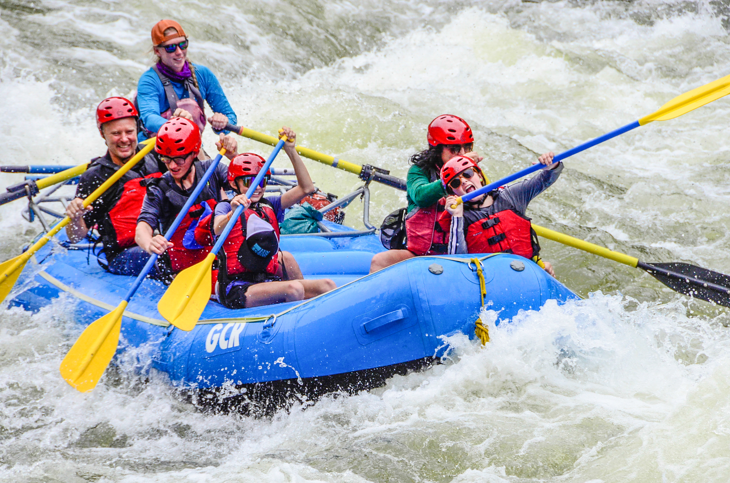 In this captivating image, a guide expertly navigates a full boat of guests through the exhilarating Shoshone Rapids. Adorned in essential safety gear, including life jackets and helmets, the group paddles together, showcasing teamwork and skill as they conquer the rapids.