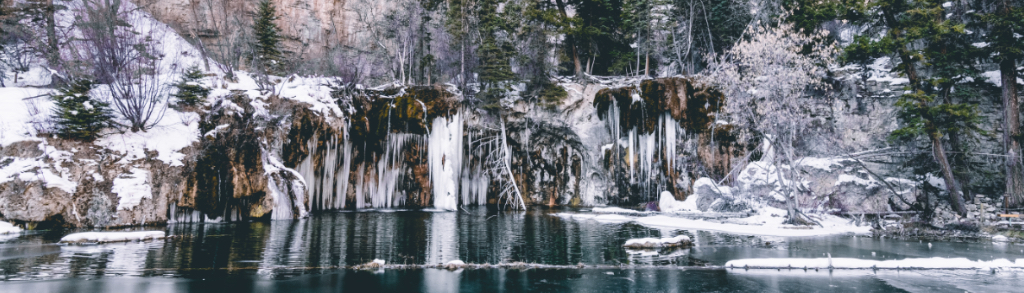 This is an image of Hanging Lake during the winter time. The water fall is frozen and you can see the reflection of the waterfall in the lake.