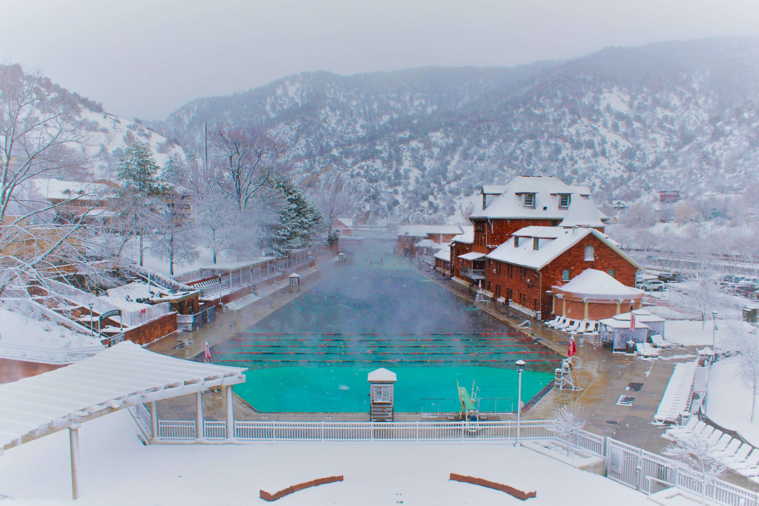 From this photo, capture the winter beauty of Glenwood Hot Springs pool from the pedestrian bridge, framed by snow-covered mountains.