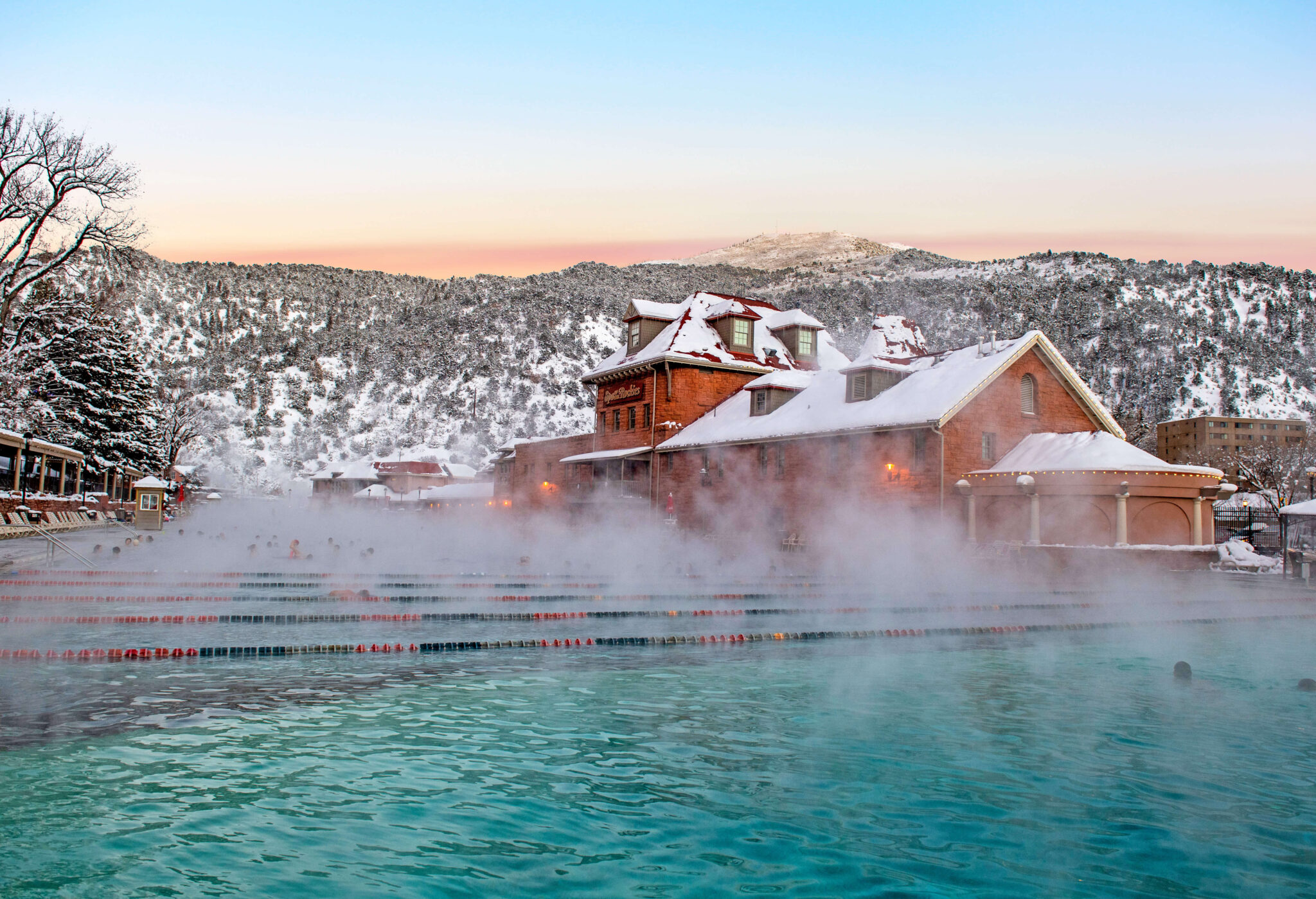 In this captivating photo, immerse yourself in the winter beauty of Glenwood Hot Springs pool from a unique poolside perspective. Situated within the pool, gaze at the snow-covered mountains, and witness the rising steam from the warm mineral waters. The scene exudes a genuine sense of peace and tranquility.
