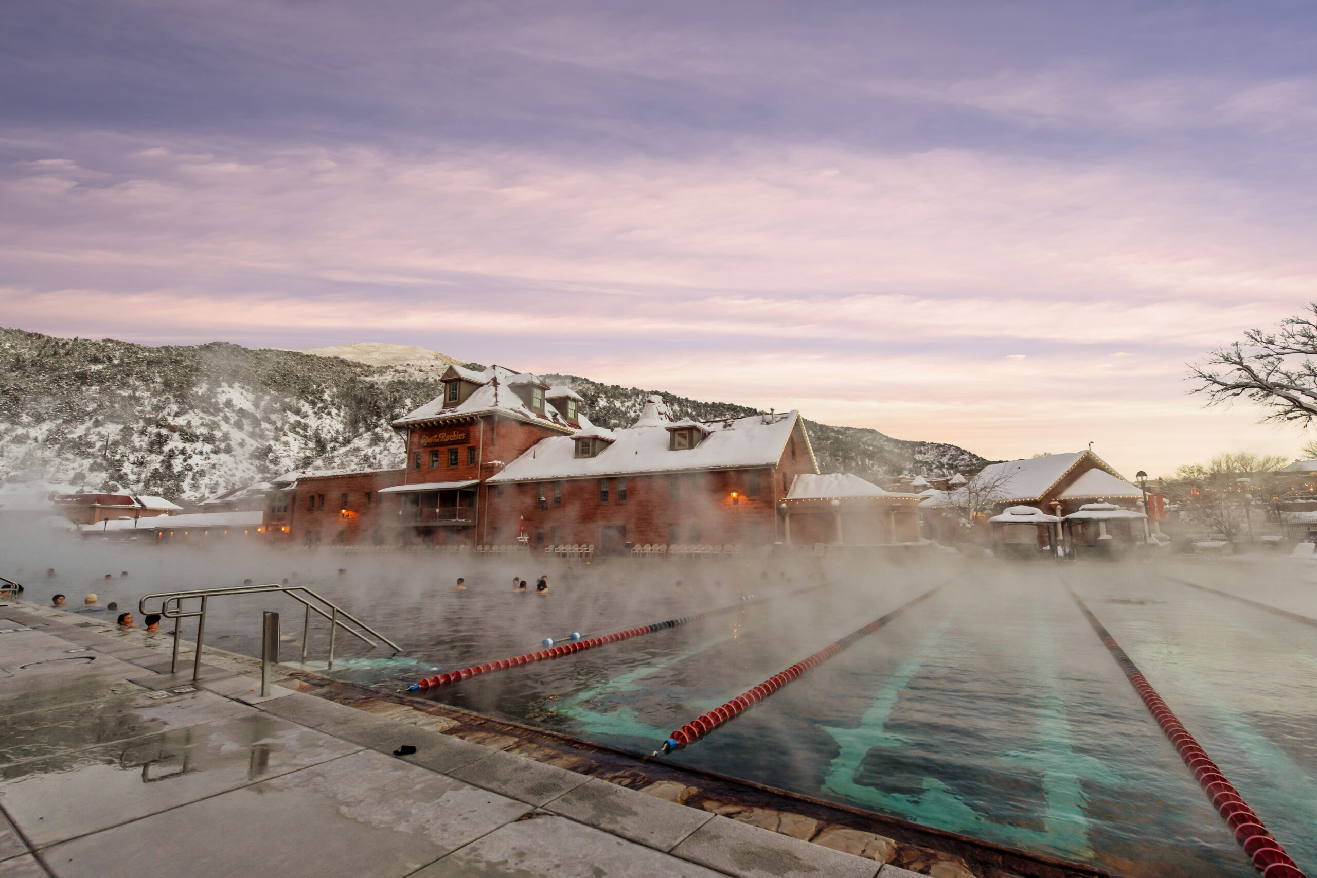 In this enchanting image, experience the winter allure of Glenwood Hot Springs pool from an exclusive poolside vantage point. Beside the pool, marvel at the snow-kissed mountains and observe the gentle steam rising from the soothing mineral waters. The scene emanates a true sense of serenity and tranquility.