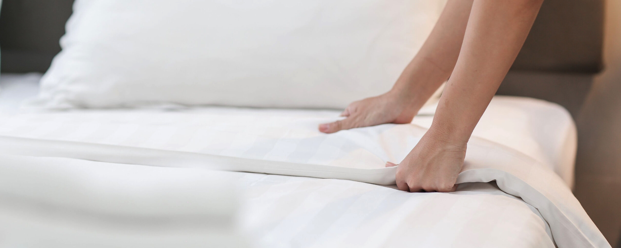 In this image, hands meticulously make a bed, adding the finishing touches with a neatly folded comforter.